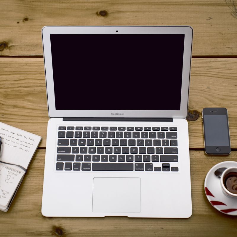 A pad and pen, a laptop and some coffee on a wooden table
